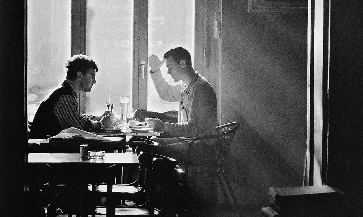 älteres schwarz/weiß-Foto: zwei Männer sitzen am Tage in einem Restaurant und sind konzentriert im Gespräch.