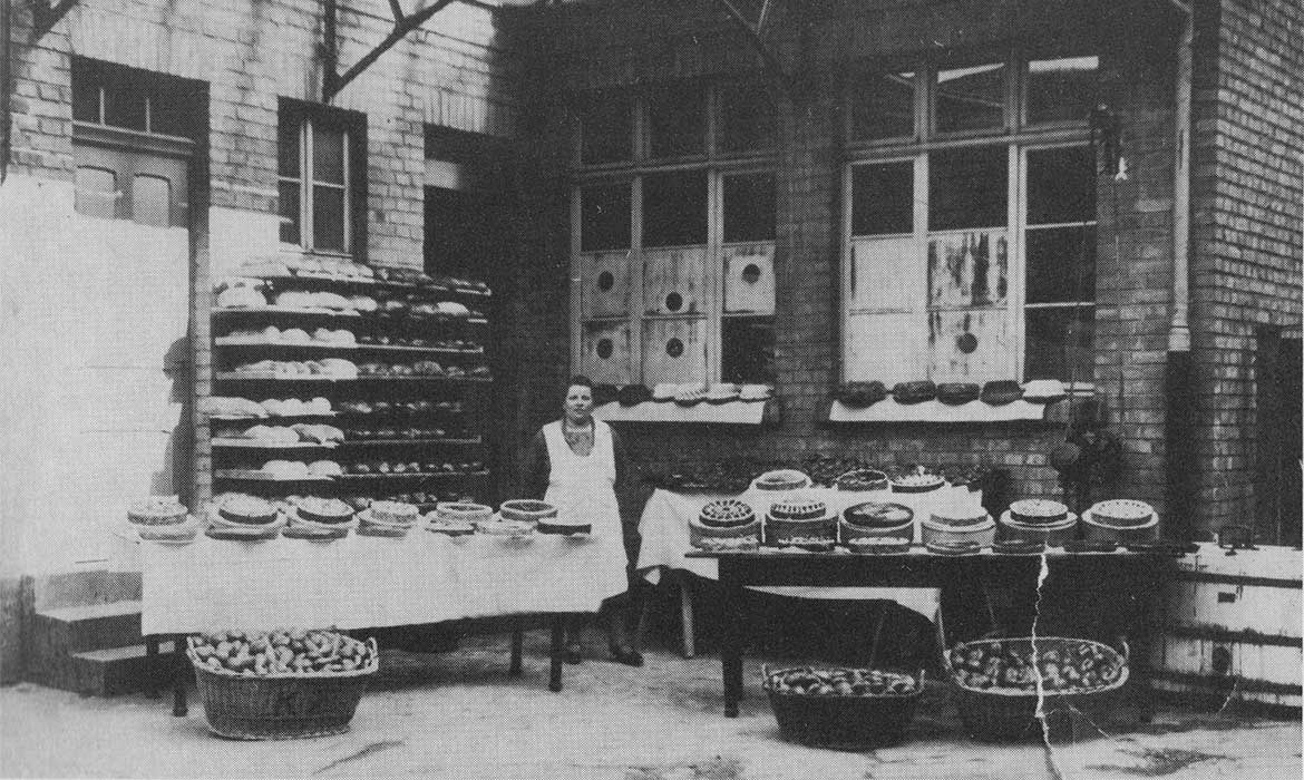 historisches Foto: eine Bäckerin präsentiert und verkauft Kuchen und Brot in einem Hinterhof.