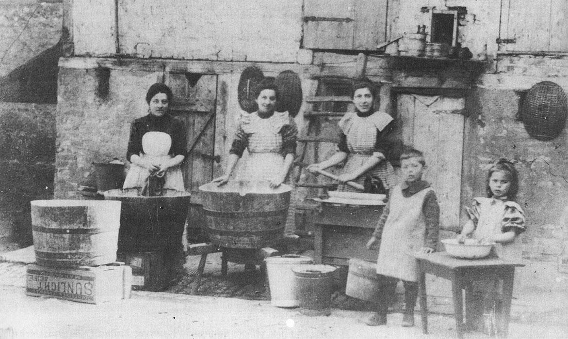 historisches Foto: drei Frauen waschen Wäsche in alten großen Kolzkübeln und zwei Mädchen waschen in einer kleinen Emailschüssel.