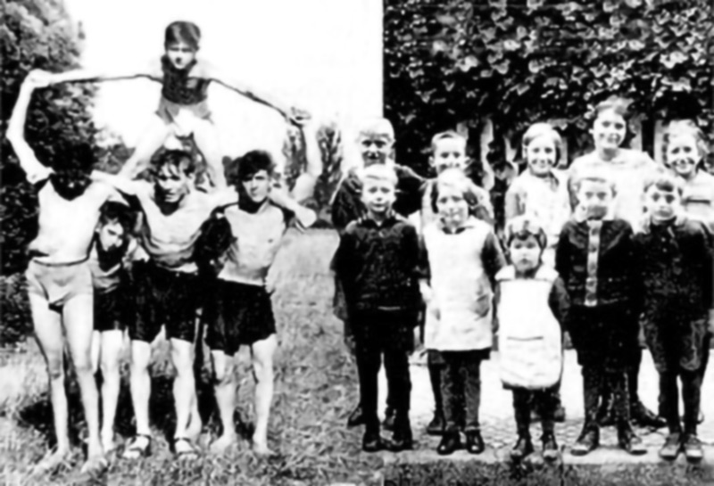 altes Foto: links eine Gruppe von Jungen in Boxer shorts, die eine Pyramide bilden, rechts eine Gruppe Mädchen und Jungen in „artiger“ Haltung und Kleidung.